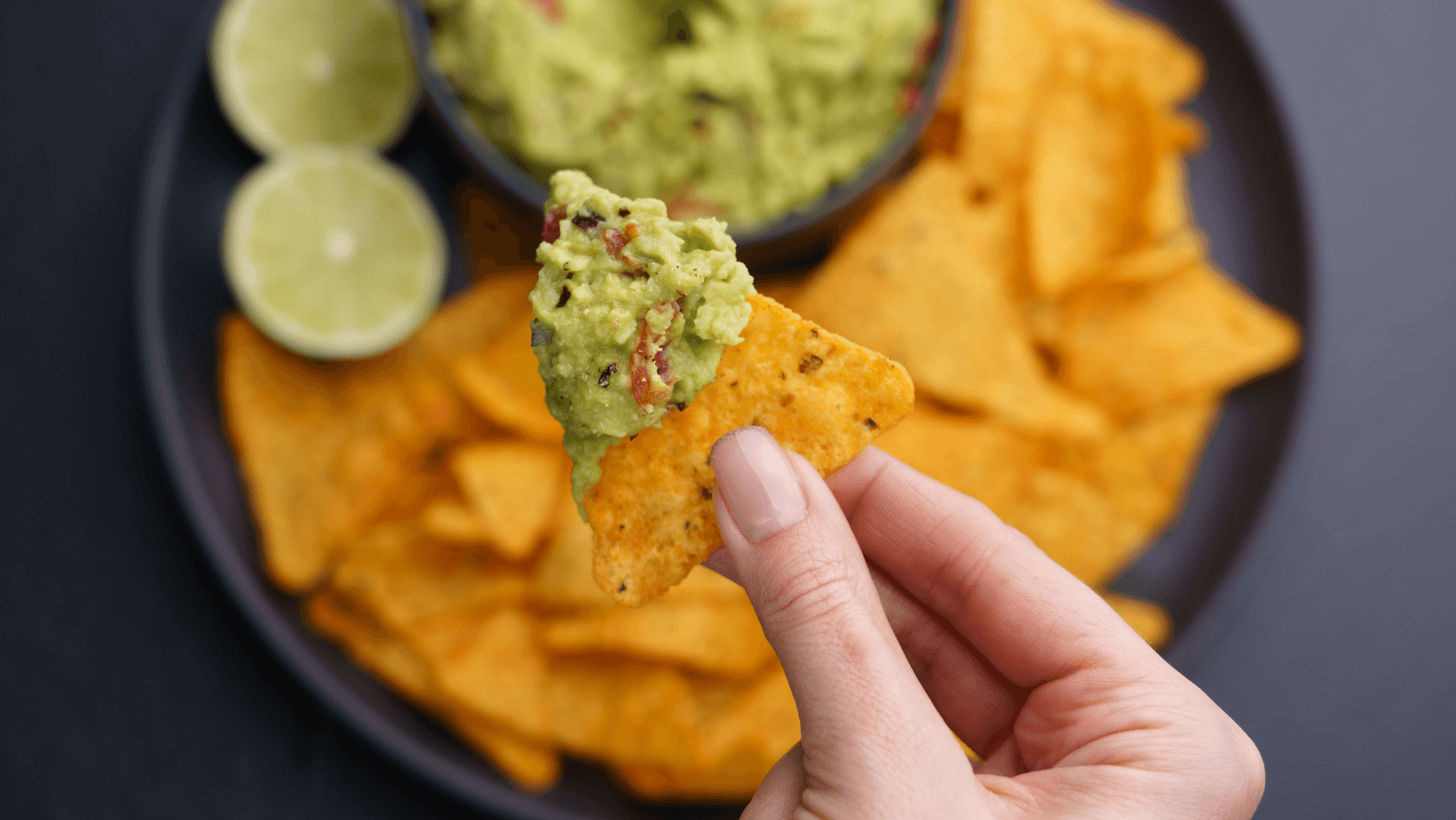 Closeup of woman hand with tortilla chips or nachos with fresh tasty guacamole dip