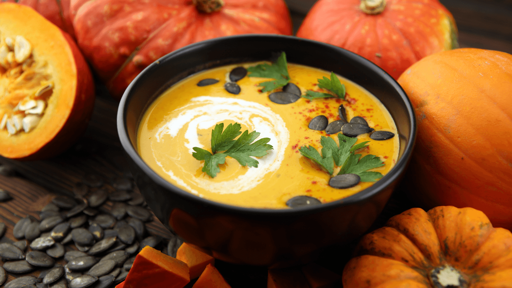 Roasted pumpkin and carrot soup with cream and pumpkin seeds on wooden background.