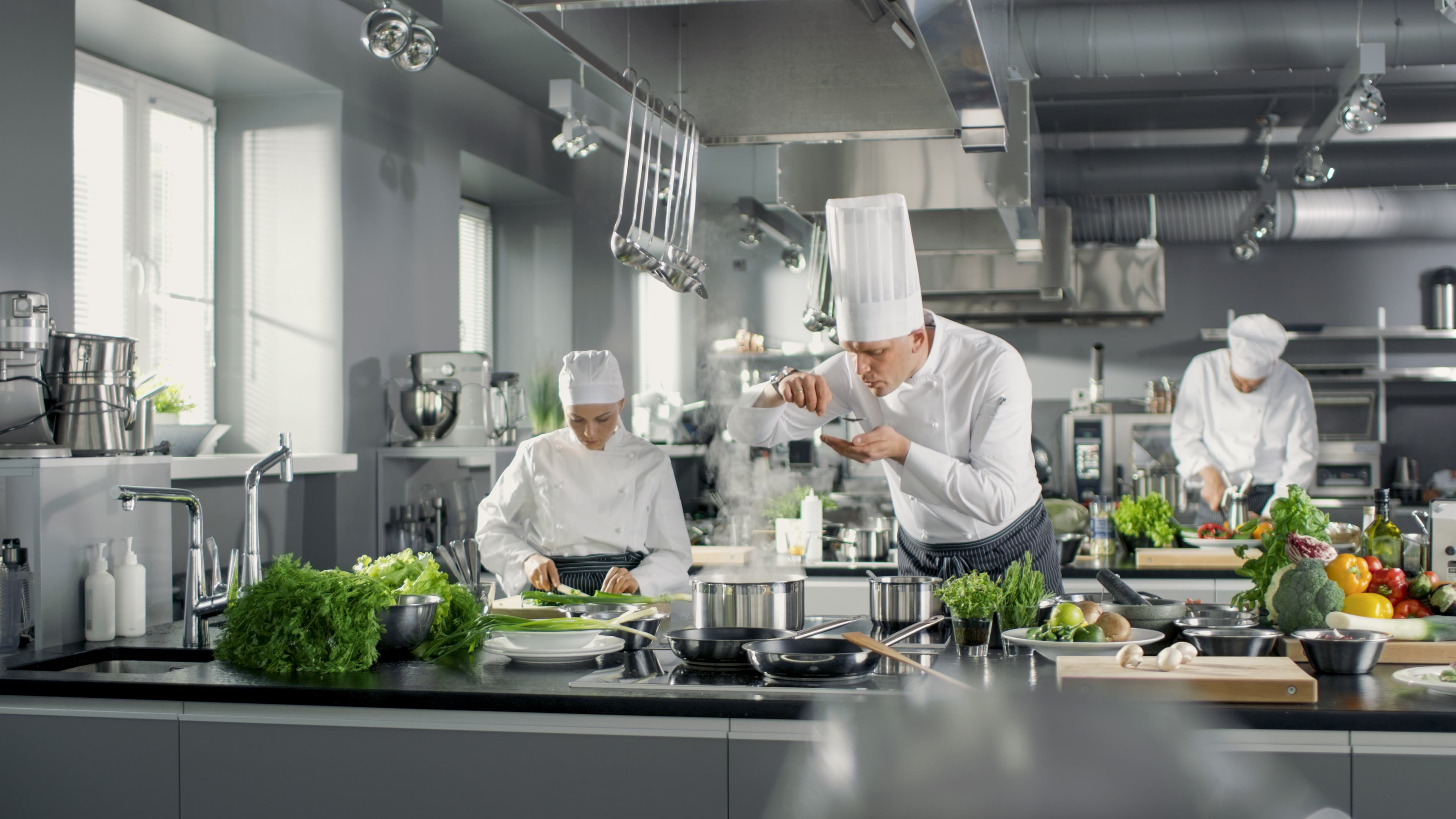 Head Chef works in a stainless steel kitchen with his staff