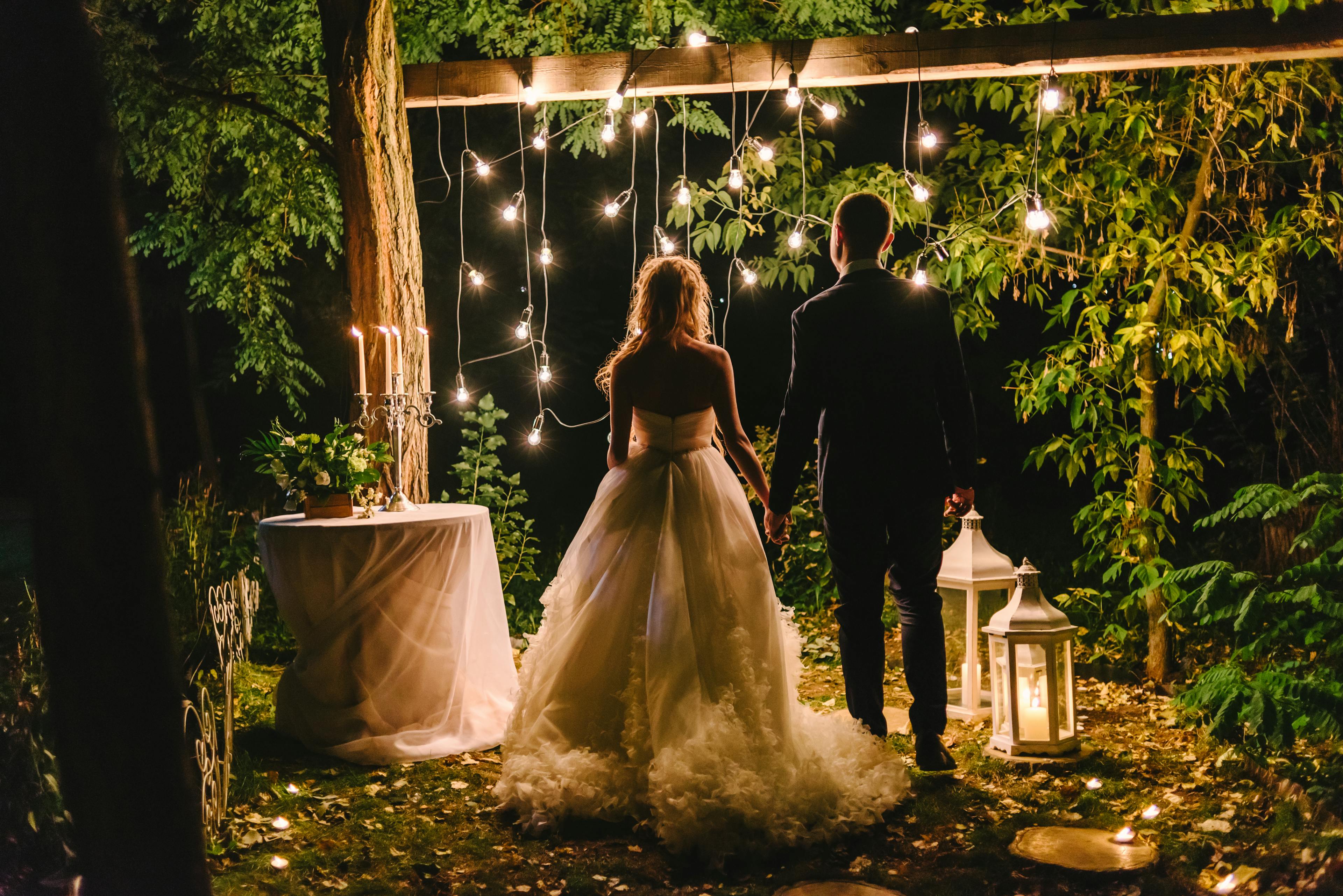 bride and groom standing together holding hands at night in front of string lights